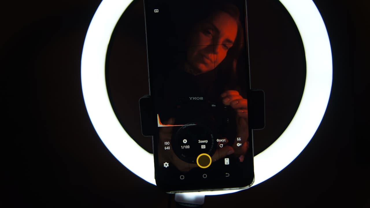 Content creator filming herself on a smartphone mounted inside a glowing ring light