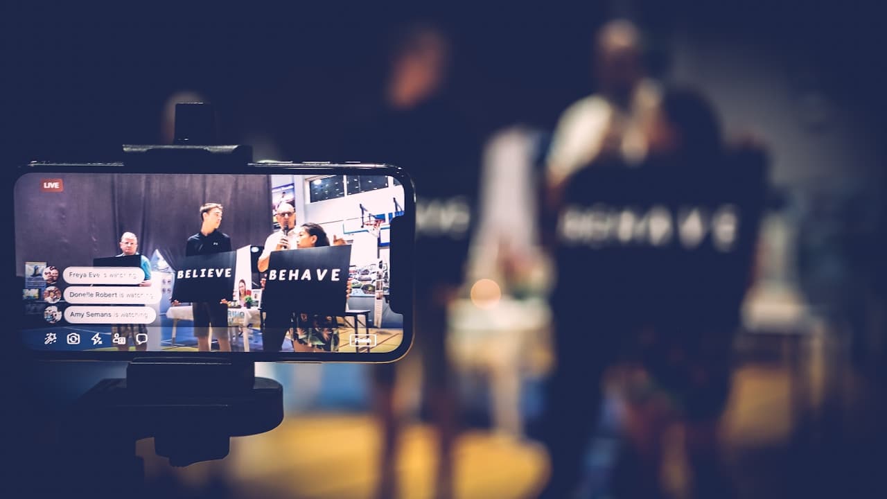 Smartphone on a tripod live streaming a presenter speaking to people on stage
