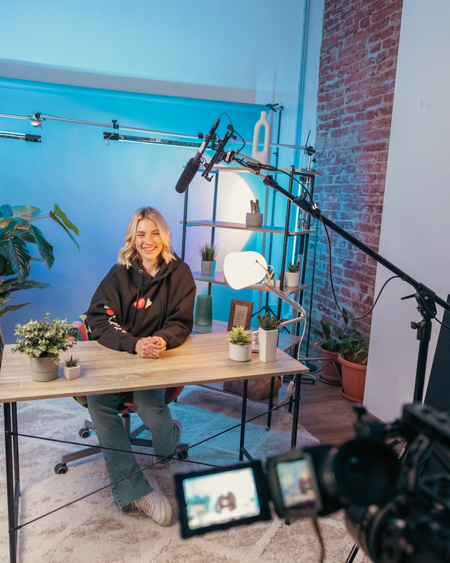 Host seated at a desk on a studio set, filmed by a camera